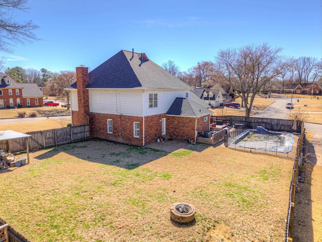 view of side of property featuring a patio, a fenced backyard, a chimney, a yard, and brick siding