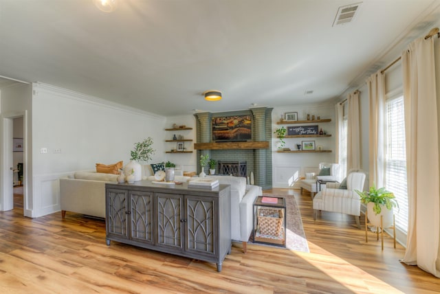 living room featuring a fireplace, crown molding, visible vents, and wood finished floors