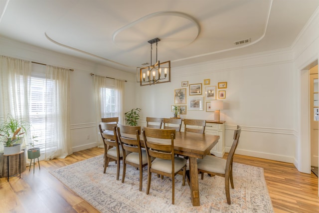 dining area with visible vents, crown molding, light wood finished floors, and an inviting chandelier