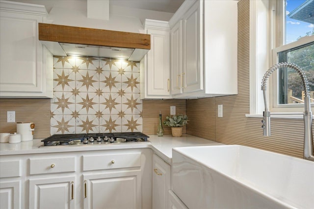 kitchen featuring range hood, stainless steel gas cooktop, white cabinets, and backsplash