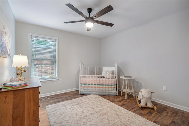 bedroom with visible vents, a crib, baseboards, and wood finished floors