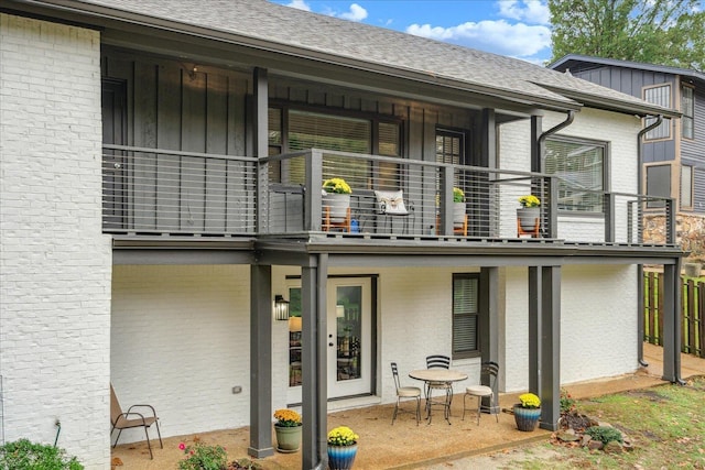 rear view of house with a patio, a balcony, brick siding, a shingled roof, and board and batten siding