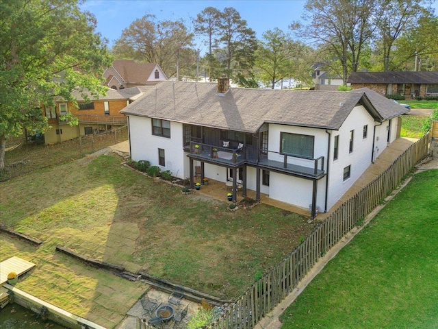 rear view of property featuring roof with shingles, a yard, a chimney, fence, and a balcony