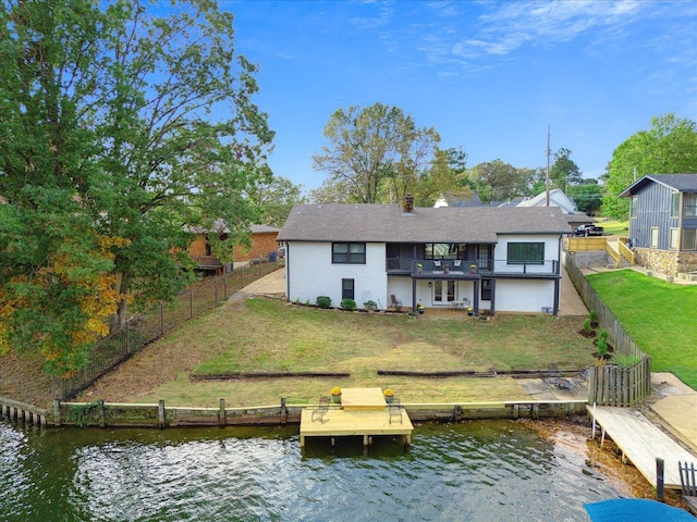 rear view of property with a water view, a balcony, a fenced backyard, and a lawn