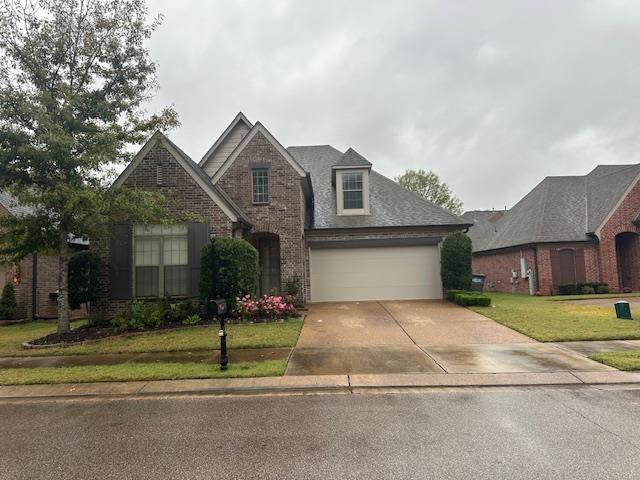 traditional-style home with driveway, brick siding, roof with shingles, and a front yard