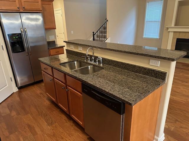 kitchen with appliances with stainless steel finishes, dark wood finished floors, a sink, and a center island with sink