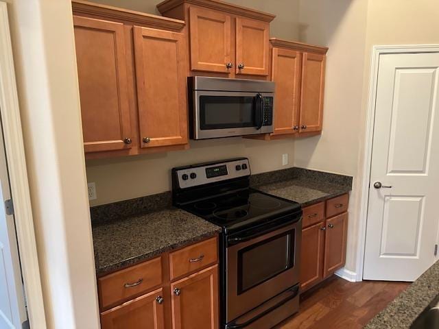 kitchen with dark stone counters, stainless steel appliances, dark wood-style floors, and brown cabinets