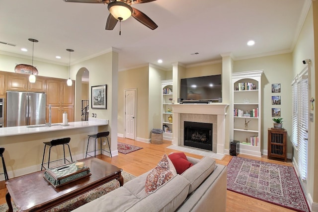 living area with ceiling fan, a tile fireplace, visible vents, and light wood-style floors