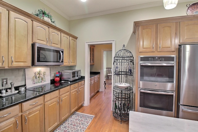 kitchen featuring dark stone counters, decorative backsplash, stainless steel appliances, crown molding, and light wood-style floors