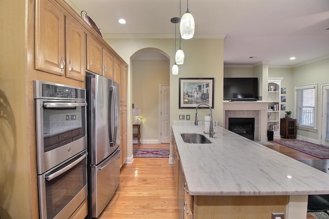 kitchen with appliances with stainless steel finishes, light wood-style floors, open floor plan, a sink, and light stone countertops