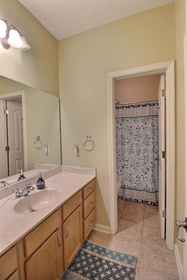 full bathroom featuring toilet, vanity, a textured ceiling, tile patterned flooring, and baseboards