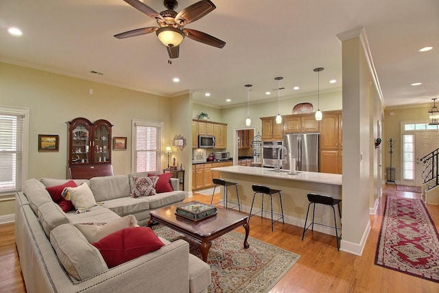 living room featuring a healthy amount of sunlight, light wood-style flooring, visible vents, and ornamental molding