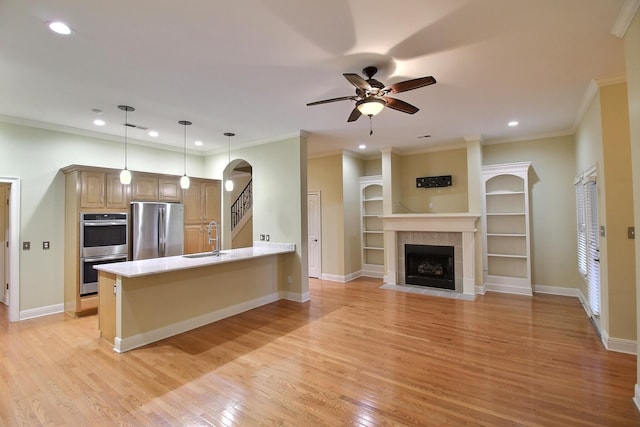 kitchen featuring a tile fireplace, light wood-style flooring, appliances with stainless steel finishes, a peninsula, and a sink