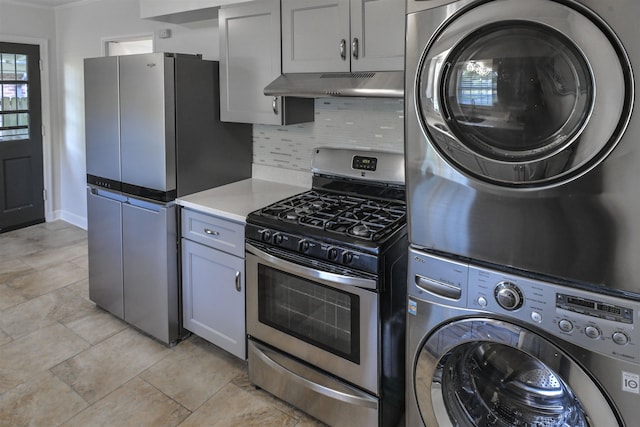 kitchen with under cabinet range hood, stacked washer / dryer, light countertops, appliances with stainless steel finishes, and backsplash