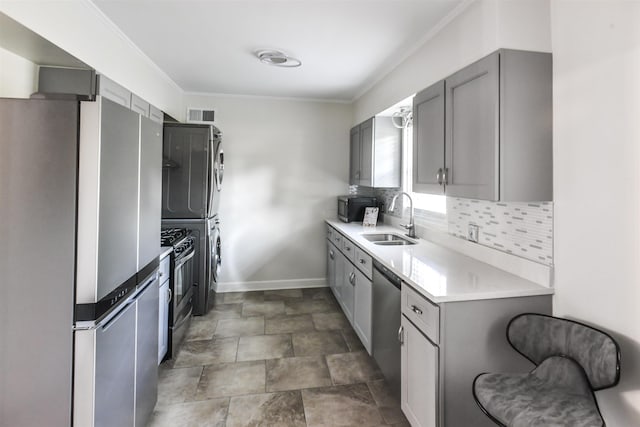 kitchen featuring stainless steel appliances, stacked washer / drying machine, gray cabinets, backsplash, and a sink