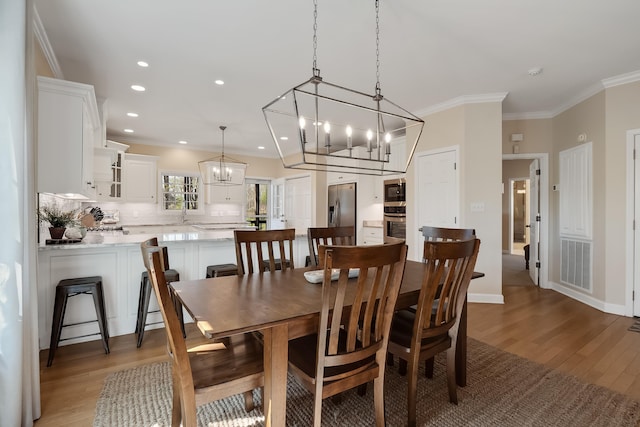 dining room with ornamental molding, visible vents, a notable chandelier, and light wood-style flooring