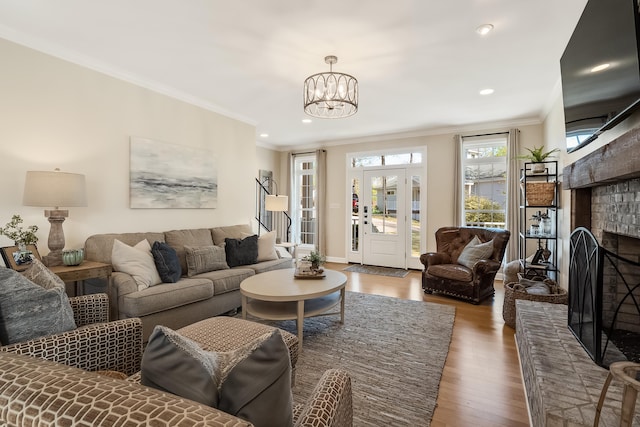 living area featuring stairway, wood finished floors, an inviting chandelier, crown molding, and a brick fireplace