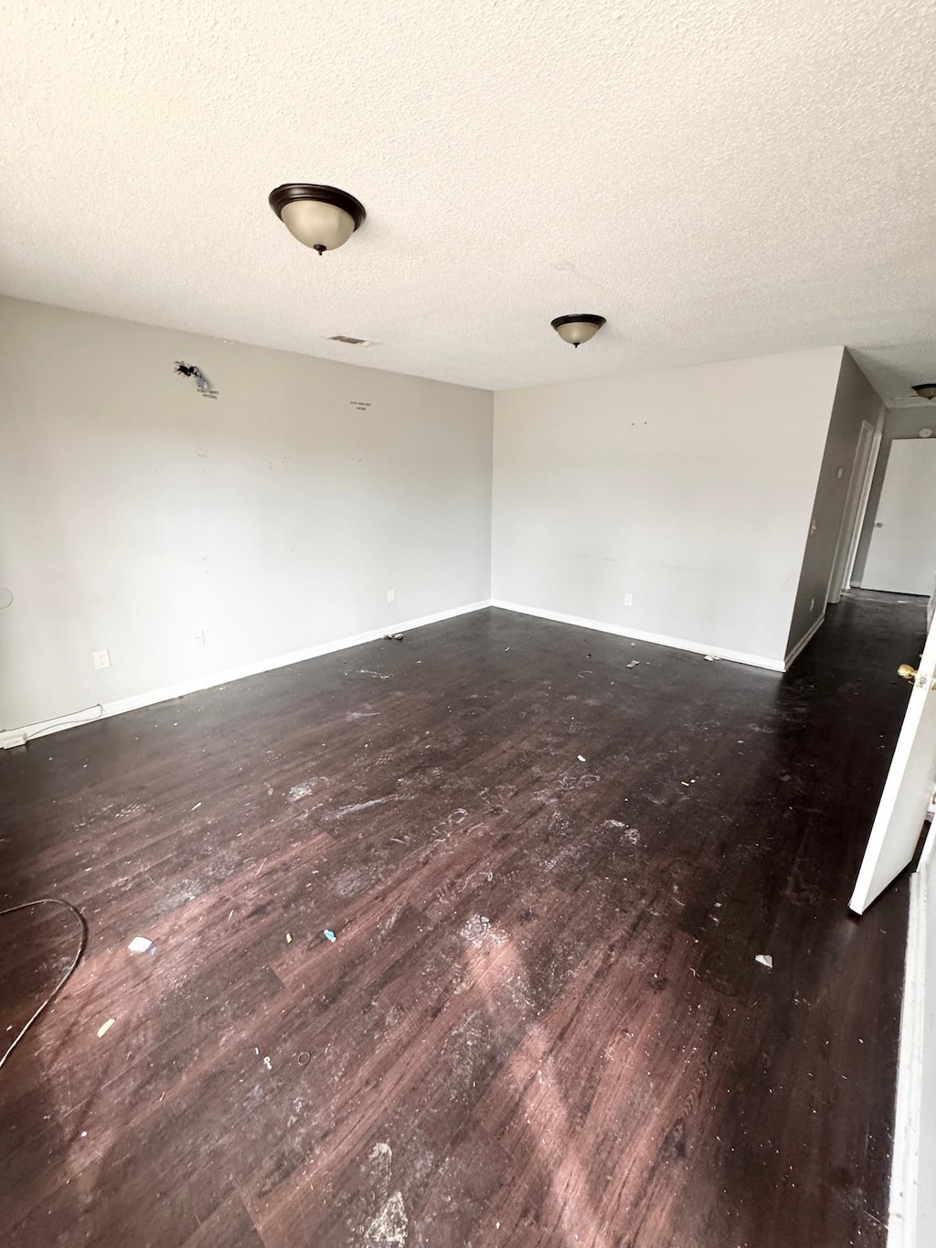 unfurnished room with a textured ceiling, baseboards, and wood finished floors