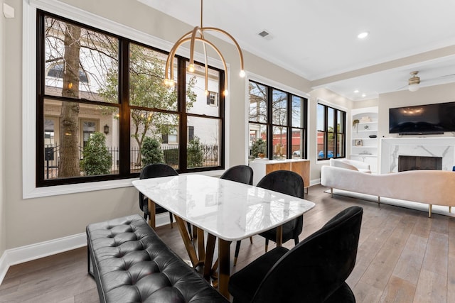 dining space with baseboards, visible vents, wood finished floors, built in shelves, and a high end fireplace