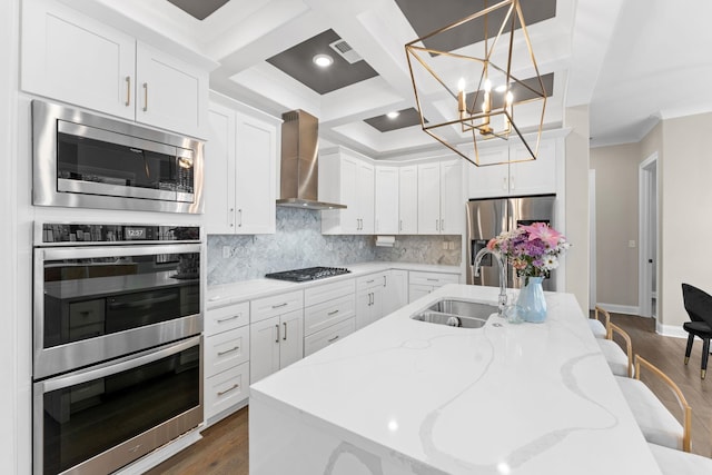 kitchen featuring a sink, white cabinets, wall chimney range hood, appliances with stainless steel finishes, and backsplash