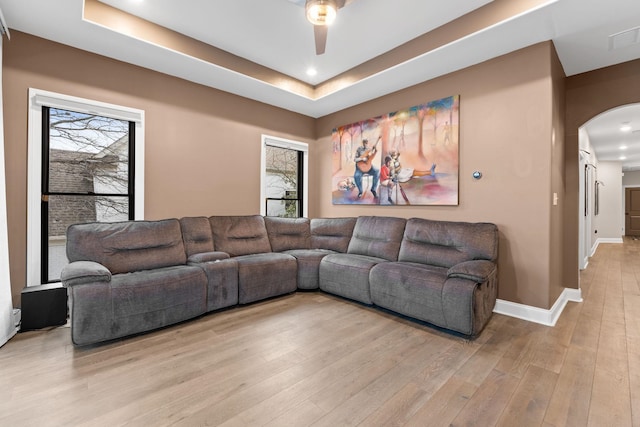 living room featuring light wood-style floors, baseboards, arched walkways, and a raised ceiling