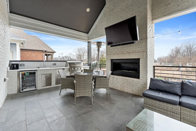 view of patio featuring wine cooler, outdoor dining area, area for grilling, and an outdoor living space with a fireplace