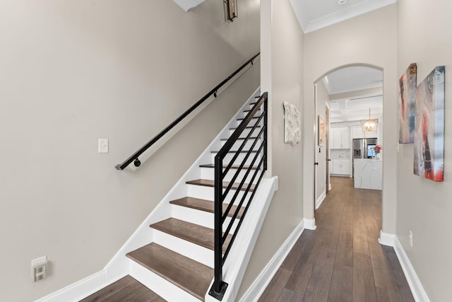 stairs featuring arched walkways, ornamental molding, hardwood / wood-style flooring, and baseboards