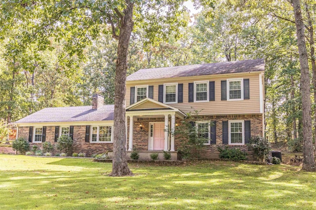 colonial house featuring brick siding, a front lawn, and a chimney