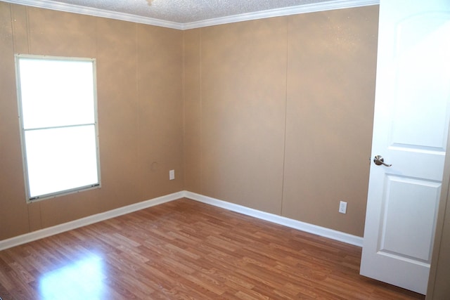 empty room with a textured ceiling, baseboards, crown molding, and wood finished floors