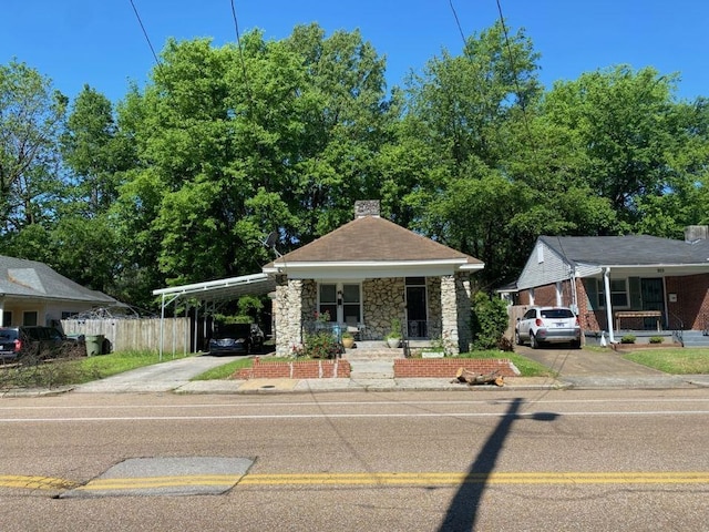 bungalow with an attached carport, stone siding, a chimney, and concrete driveway