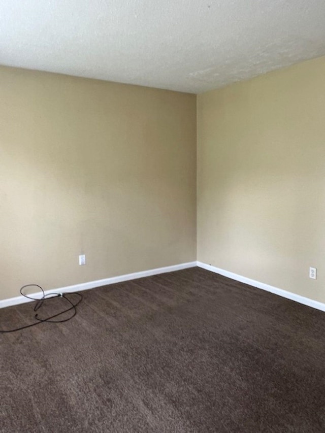 unfurnished room with a textured ceiling, dark carpet, and baseboards