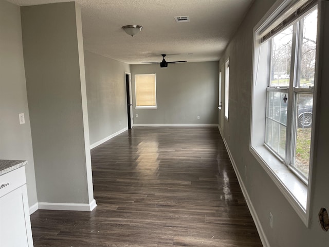 spare room featuring ceiling fan, a textured ceiling, visible vents, baseboards, and dark wood-style floors