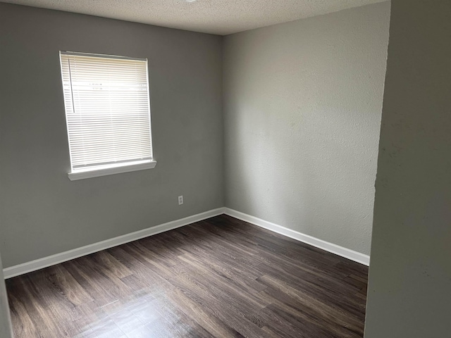 empty room with a textured ceiling, baseboards, and dark wood-type flooring