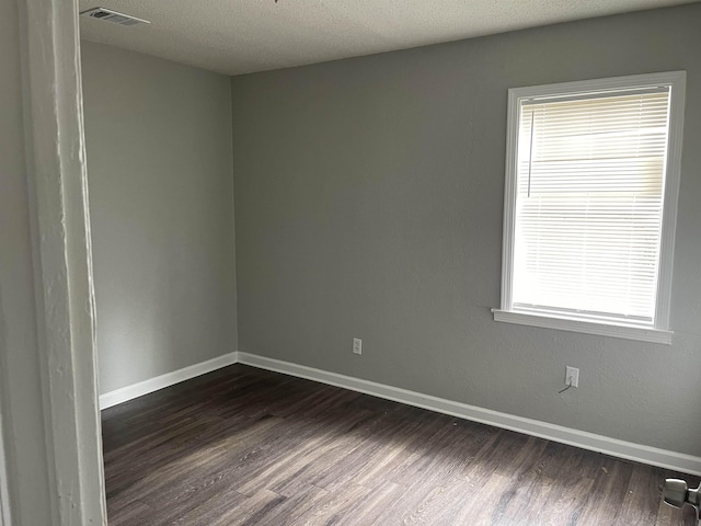 unfurnished room featuring baseboards, visible vents, dark wood finished floors, and a wealth of natural light