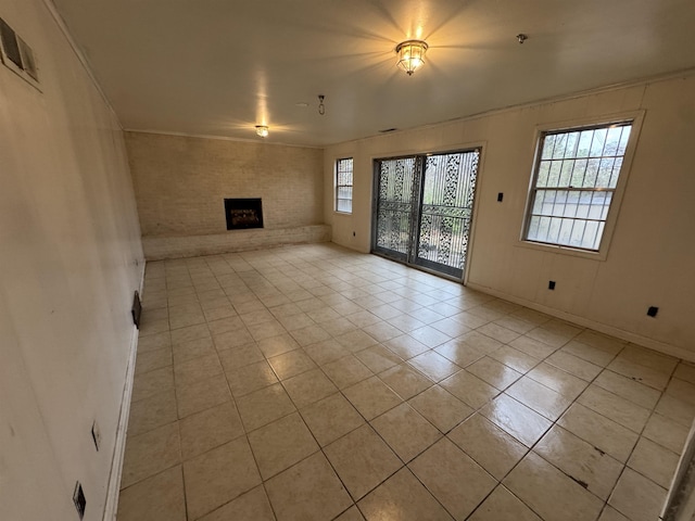 unfurnished living room featuring a large fireplace, plenty of natural light, brick wall, and light tile patterned flooring