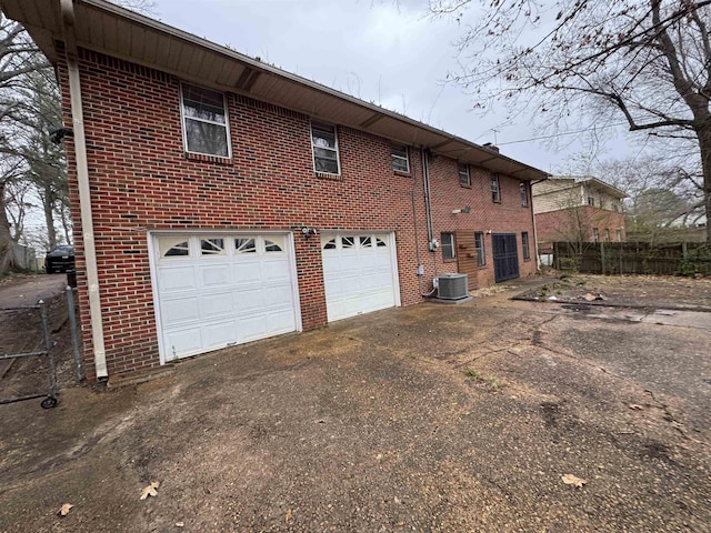 rear view of house featuring driveway, a garage, fence, central AC, and brick siding