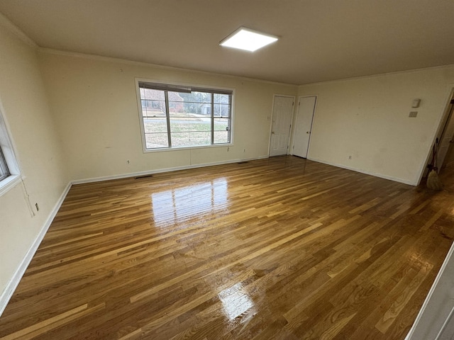 spare room with visible vents, crown molding, baseboards, and wood finished floors