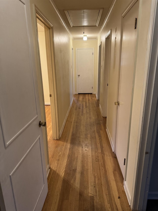 hallway featuring baseboards, wood finished floors, attic access, and crown molding