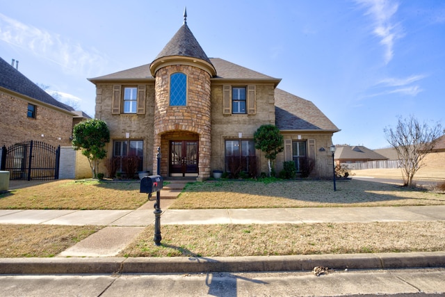 french country inspired facade featuring stone siding, a shingled roof, a gate, and french doors