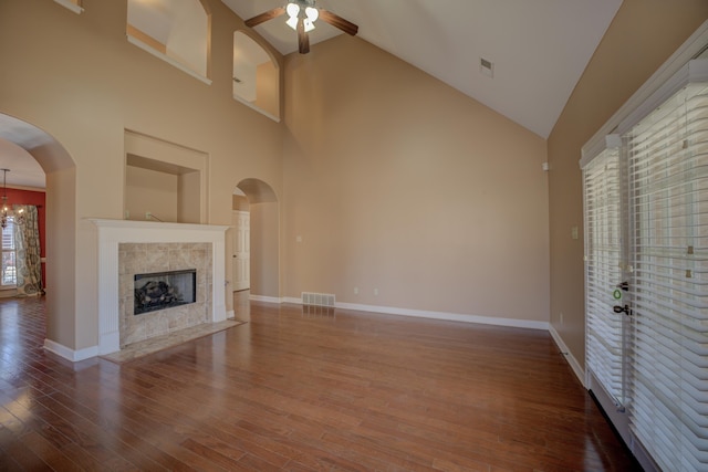 unfurnished living room featuring baseboards, arched walkways, a tile fireplace, wood finished floors, and ceiling fan with notable chandelier