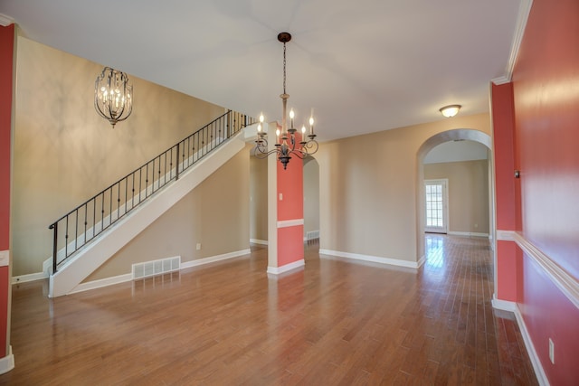 interior space featuring arched walkways, a notable chandelier, wood finished floors, visible vents, and baseboards