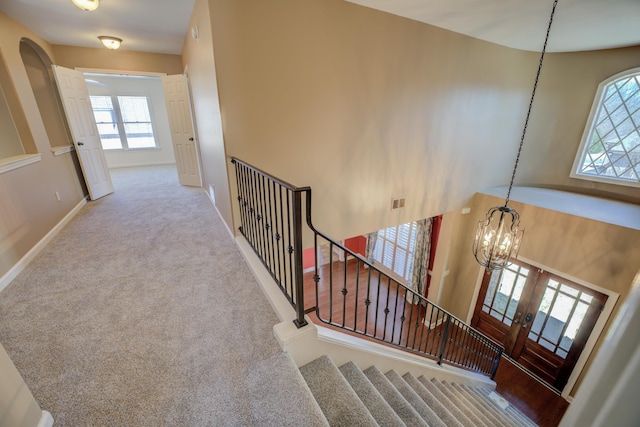 stairs featuring a chandelier, arched walkways, carpet floors, visible vents, and baseboards