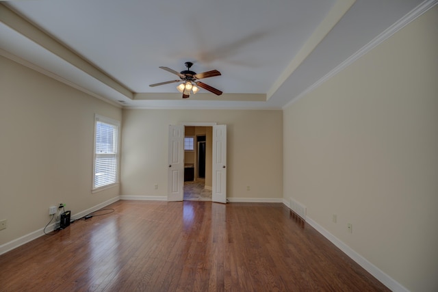 empty room with baseboards, a raised ceiling, ceiling fan, wood finished floors, and crown molding