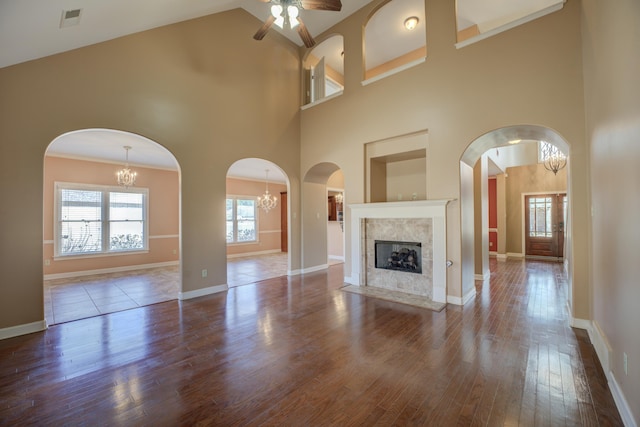 unfurnished living room featuring a fireplace, visible vents, wood finished floors, baseboards, and ceiling fan with notable chandelier