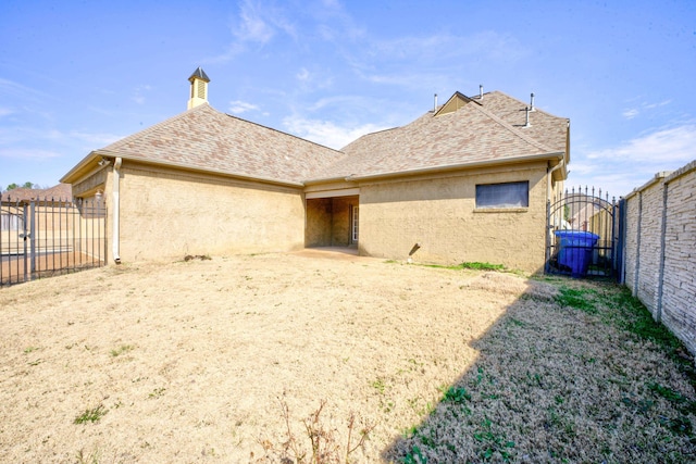 rear view of property with a shingled roof, fence, and stucco siding