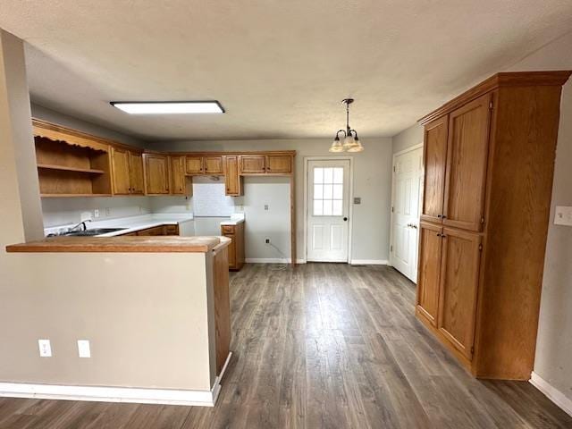 kitchen with a peninsula, baseboards, brown cabinetry, and dark wood-type flooring