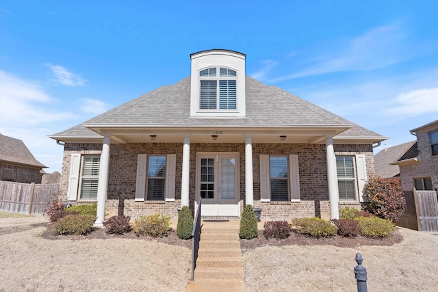 bungalow featuring covered porch, roof with shingles, fence, and brick siding