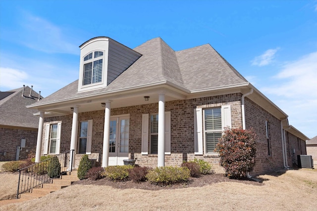 view of front of home with a shingled roof, french doors, brick siding, and central AC unit