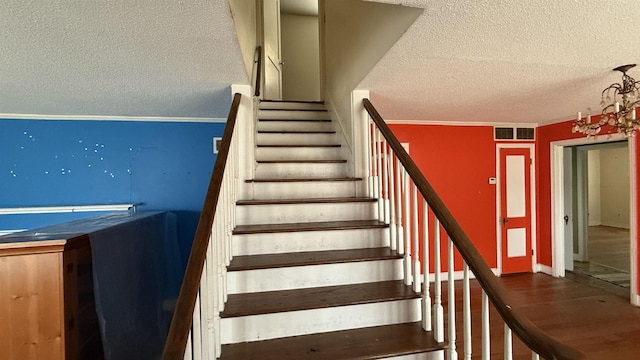 staircase featuring a textured ceiling, ornamental molding, and visible vents