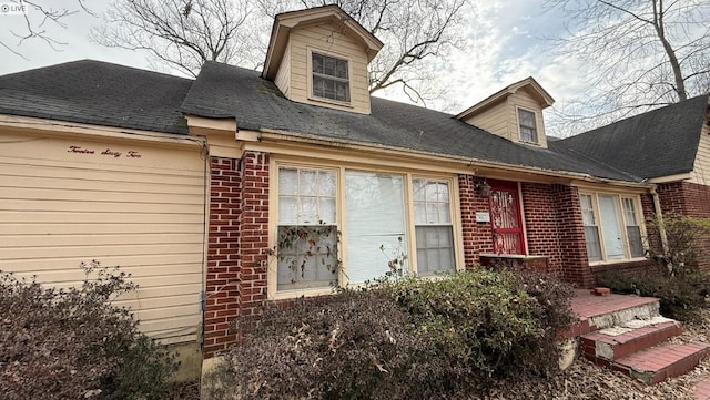 doorway to property with brick siding and a shingled roof